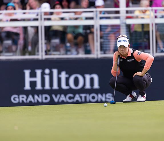 Japanese professional golfer Nasa Hataoka lining up a putt in from of a Hilton Grand Vacations sponsor board.