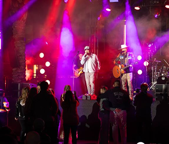A live band play on stage with pink and purple lights in the background.