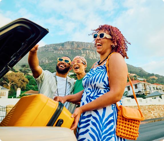 Three people unloading their luggage from the trunk of a Taxi and laughing.